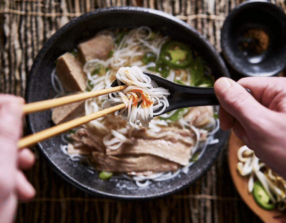 hands using a Chirenge and chop sticks over a bowl of pho